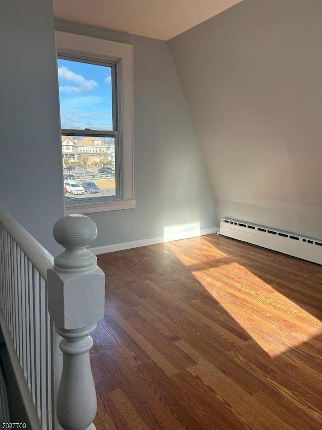 additional living space with lofted ceiling, a baseboard heating unit, and dark wood-type flooring