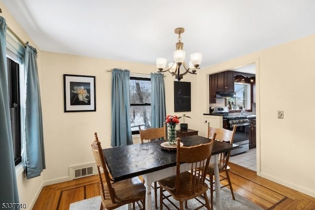 dining space featuring baseboards, light wood-style flooring, visible vents, and a notable chandelier