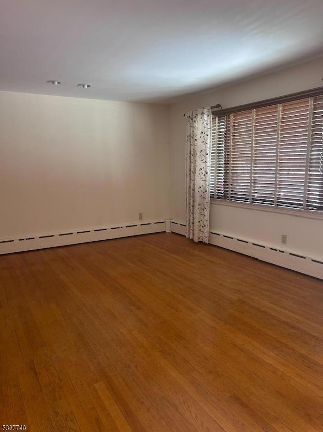 unfurnished room featuring hardwood / wood-style flooring and a baseboard heating unit