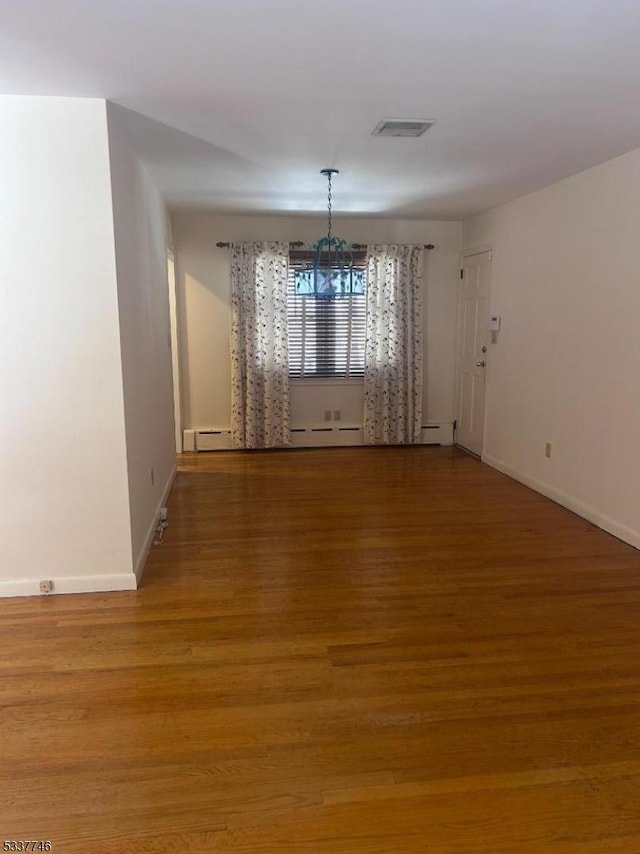 unfurnished dining area with hardwood / wood-style floors, a chandelier, and a baseboard heating unit