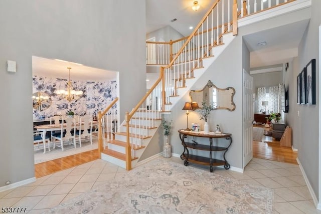 stairs featuring tile patterned flooring, a towering ceiling, baseboards, and an inviting chandelier