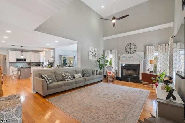 living area featuring light wood-style floors, a ceiling fan, a fireplace with raised hearth, and a wealth of natural light