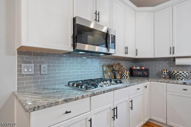 kitchen featuring white cabinets, light stone counters, stainless steel appliances, and backsplash