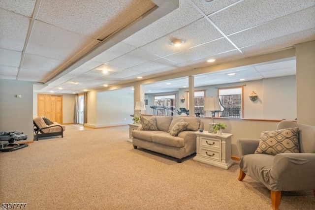 living area featuring baseboards, light carpet, and a drop ceiling