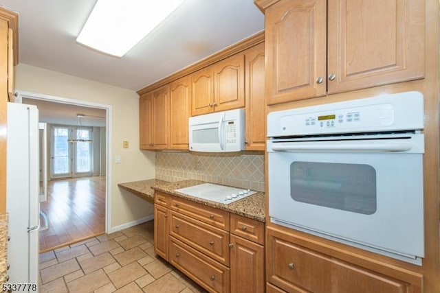 kitchen featuring tasteful backsplash, light stone countertops, and white appliances