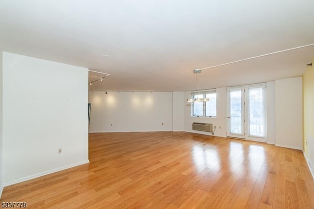 spare room featuring an inviting chandelier, a wall mounted AC, track lighting, and light wood-type flooring