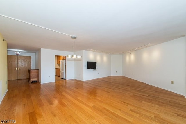 unfurnished living room featuring rail lighting and light hardwood / wood-style flooring