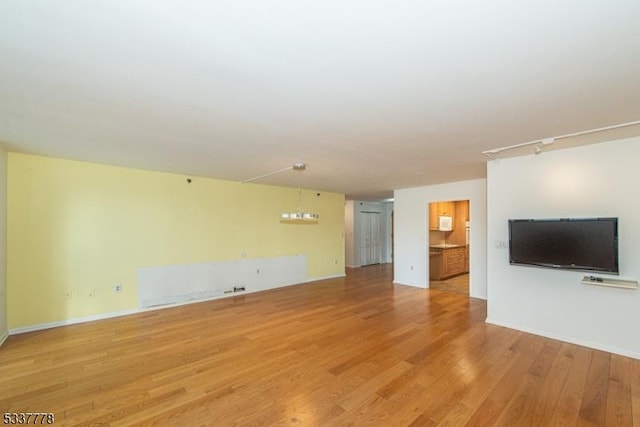 unfurnished living room featuring hardwood / wood-style flooring and rail lighting