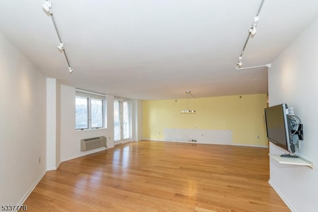 unfurnished living room with rail lighting, a wall mounted AC, and light wood-type flooring