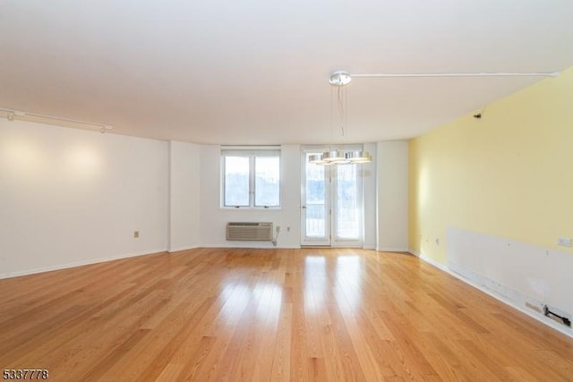 spare room featuring a notable chandelier, track lighting, a wall unit AC, and light wood-type flooring