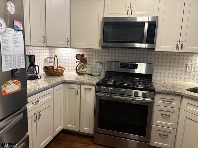 kitchen with stainless steel appliances, white cabinets, backsplash, and light stone counters