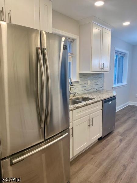 kitchen with stainless steel appliances, white cabinetry, backsplash, and light stone counters