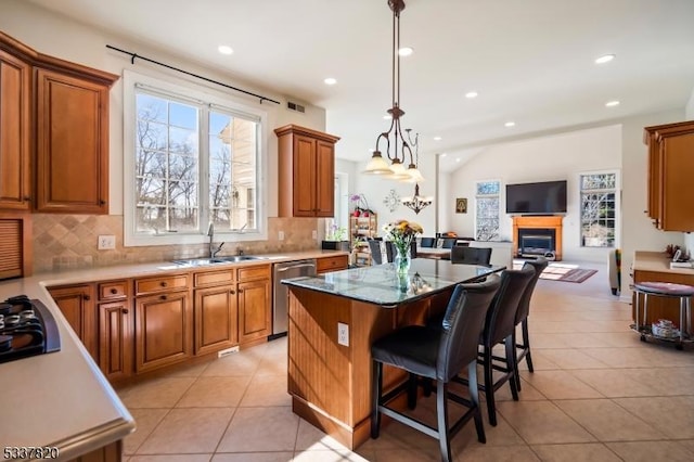 kitchen with a breakfast bar, sink, hanging light fixtures, a center island, and stainless steel dishwasher