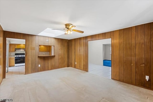 empty room with ceiling fan, a skylight, and wooden walls