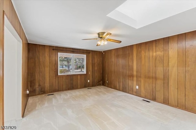 spare room with wood walls, a skylight, and visible vents