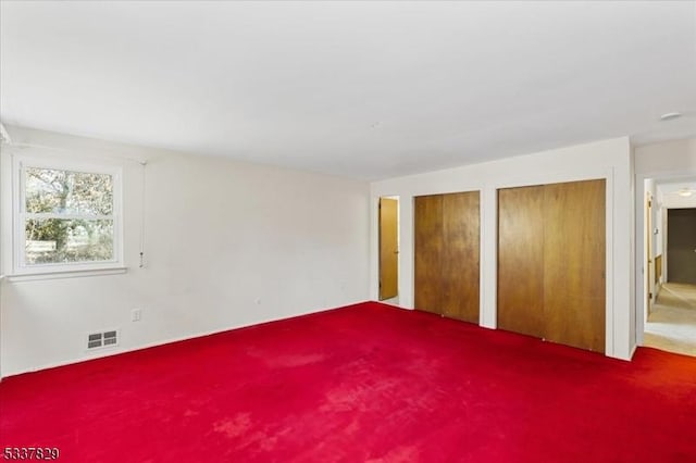 unfurnished bedroom with carpet floors, visible vents, and multiple closets