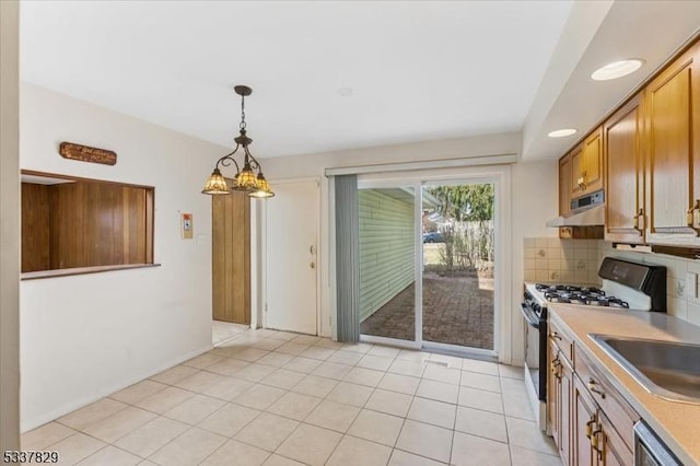 kitchen with under cabinet range hood, light countertops, backsplash, gas stove, and decorative light fixtures