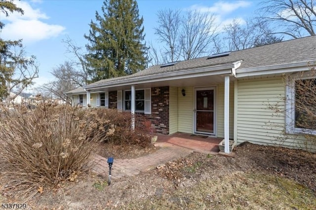 view of front of property featuring brick siding and roof with shingles