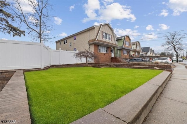 view of side of property featuring a gambrel roof, a lawn, fence, a residential view, and brick siding