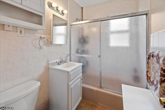 bathroom featuring toilet, tile walls, tile patterned flooring, bath / shower combo with glass door, and vanity