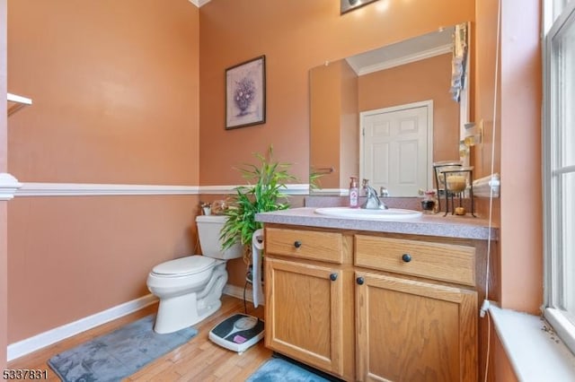 bathroom featuring toilet, wood finished floors, vanity, baseboards, and ornamental molding