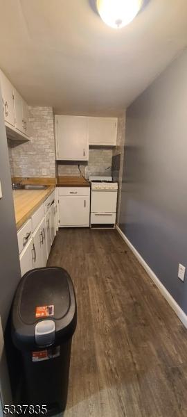 kitchen featuring stove, white cabinetry, baseboards, light countertops, and dark wood-style floors