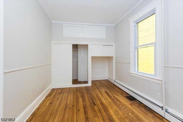 unfurnished bedroom with ornamental molding, a baseboard heating unit, and hardwood / wood-style floors