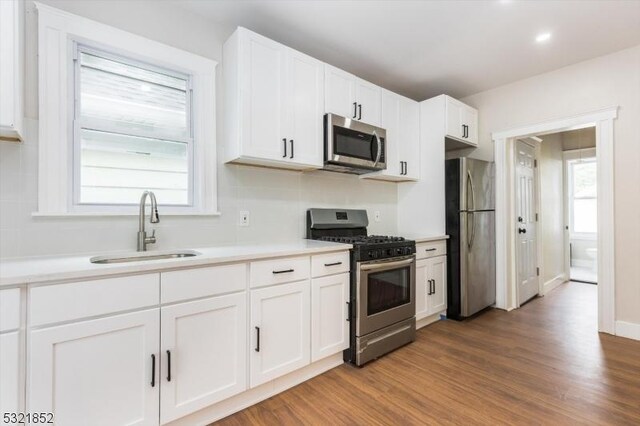 kitchen with sink, hardwood / wood-style flooring, stainless steel appliances, and white cabinets