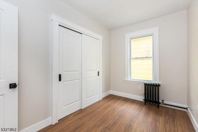 unfurnished bedroom featuring radiator heating unit, a closet, and wood-type flooring