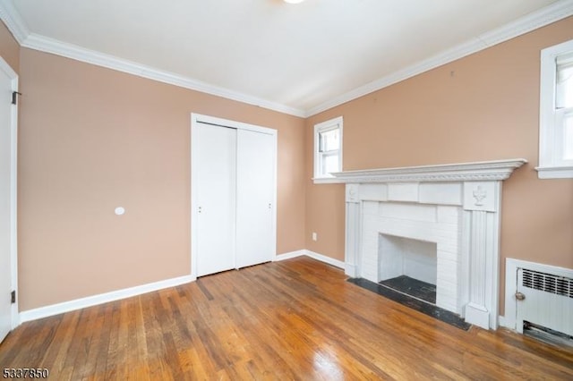 unfurnished living room with hardwood / wood-style flooring, crown molding, a brick fireplace, and radiator heating unit