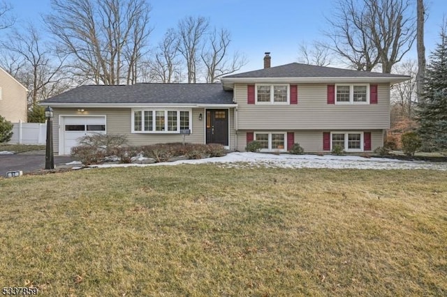 tri-level home featuring an attached garage, driveway, a chimney, and a front lawn