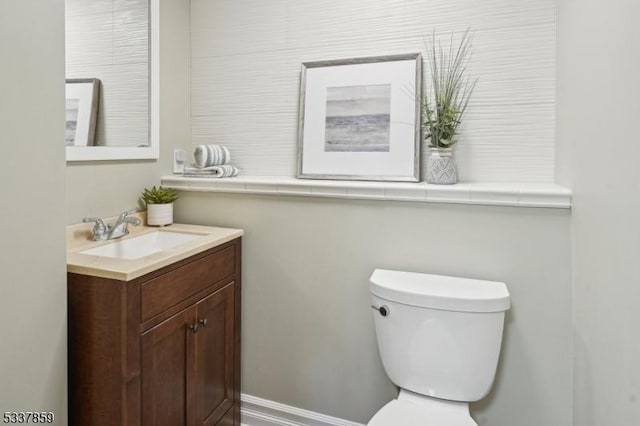 half bathroom with toilet, baseboards, and vanity