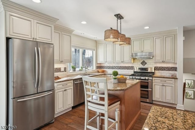 kitchen with a center island, decorative light fixtures, stainless steel appliances, light stone countertops, and under cabinet range hood