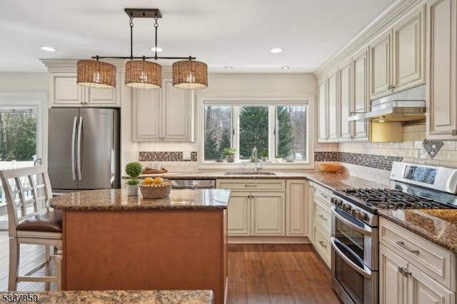 kitchen with a center island, decorative light fixtures, stainless steel appliances, stone countertops, and a sink