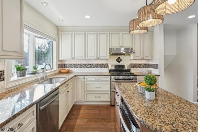 kitchen with light stone counters, decorative light fixtures, stainless steel appliances, a sink, and under cabinet range hood