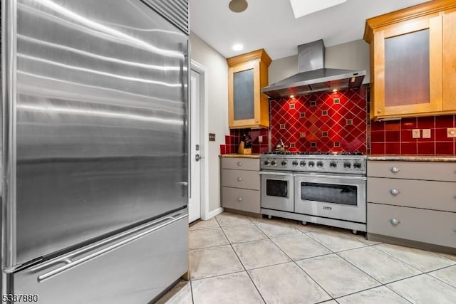 kitchen with light tile patterned floors, premium appliances, wall chimney range hood, and tasteful backsplash