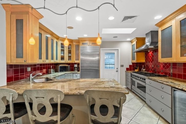 kitchen with a peninsula, a sink, visible vents, high quality appliances, and wall chimney range hood