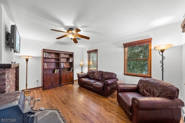 living room featuring a ceiling fan, a fireplace, and wood finished floors