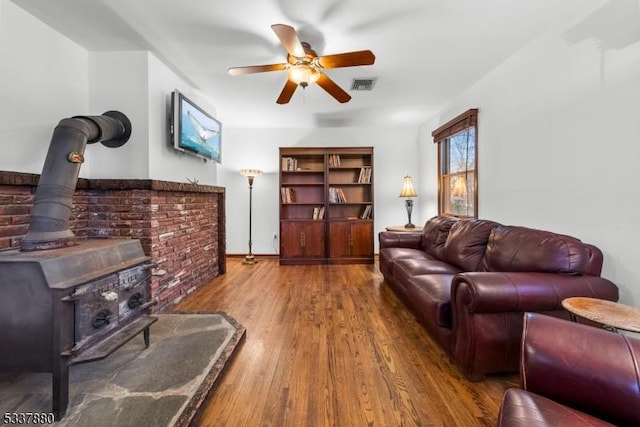 living room featuring a wood stove, wood finished floors, visible vents, and a ceiling fan