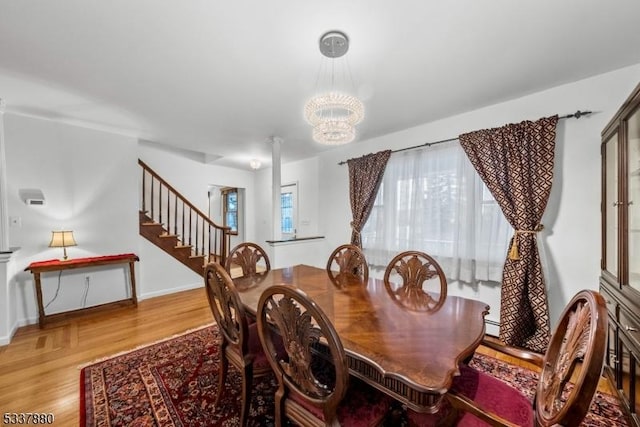 dining space featuring baseboard heating, a chandelier, light wood-type flooring, baseboards, and stairs