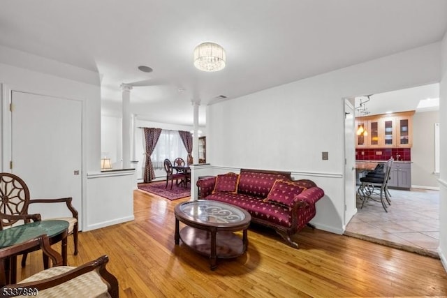 living area featuring ornate columns, light wood-style flooring, and a notable chandelier