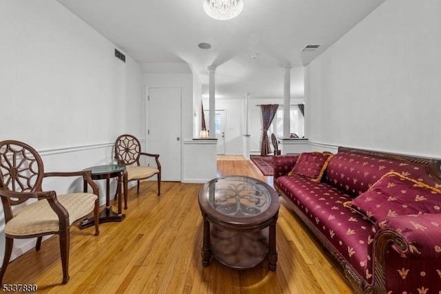 living area with ornate columns, visible vents, and wood finished floors