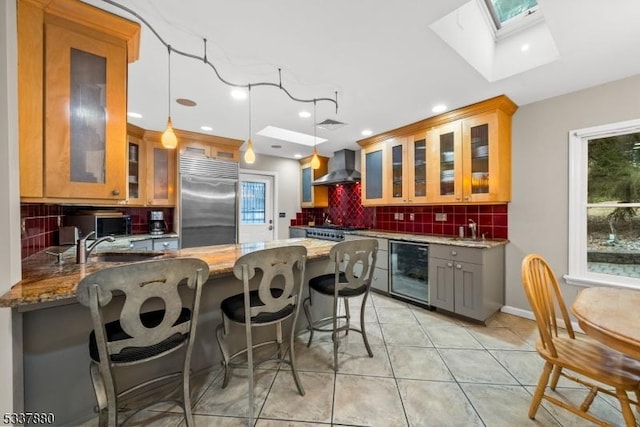 kitchen with beverage cooler, light stone counters, a peninsula, stainless steel appliances, and wall chimney range hood