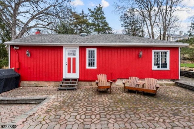 rear view of property featuring entry steps, a patio area, a chimney, and roof with shingles