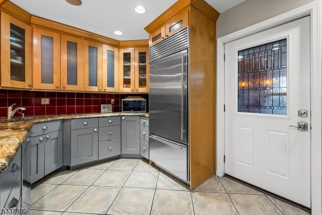 kitchen with light tile patterned floors, tasteful backsplash, gray cabinetry, light stone countertops, and stainless steel built in refrigerator