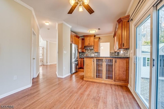 kitchen featuring ornamental molding, stainless steel refrigerator with ice dispenser, under cabinet range hood, dark countertops, and brown cabinets