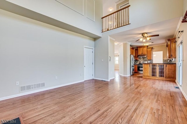 unfurnished living room featuring visible vents, a ceiling fan, light wood-style floors, crown molding, and baseboards