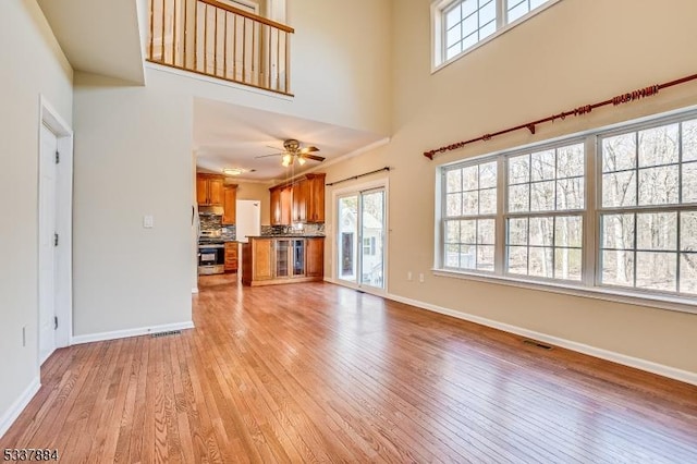 unfurnished living room with a towering ceiling, visible vents, baseboards, and light wood finished floors