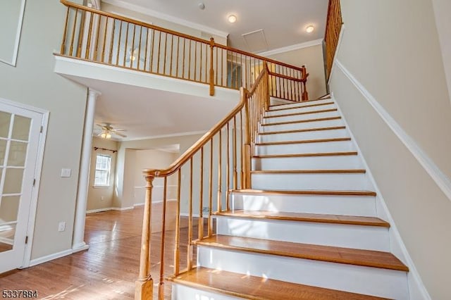 stairway featuring a ceiling fan, wood finished floors, a high ceiling, crown molding, and baseboards