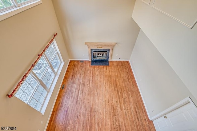 unfurnished living room with plenty of natural light, baseboards, a towering ceiling, and wood finished floors